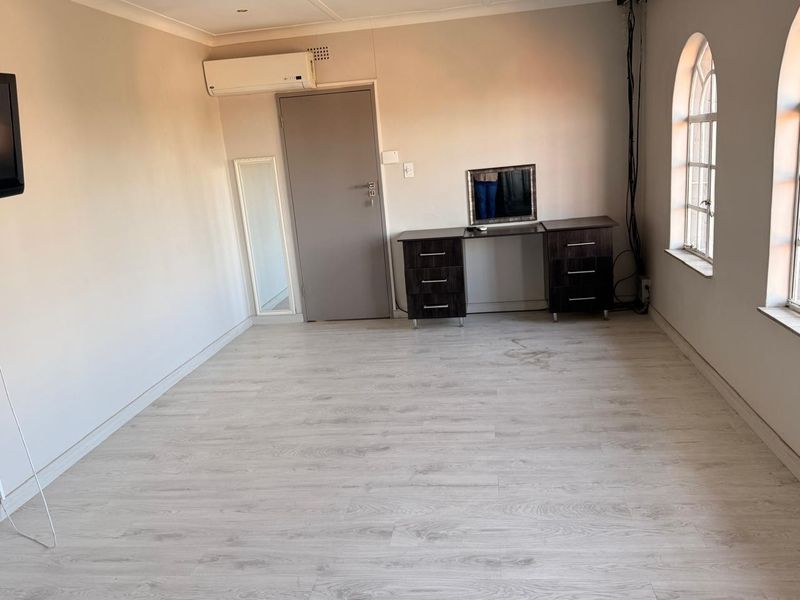 A spacious bedroom featuring light-toned laminate flooring, arched windows, and a wall-mounted air conditioning unit.