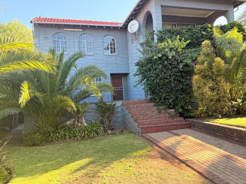 Front elevation of a two-story house featuring a brick staircase, paved walkway, and arched windows with security bars.