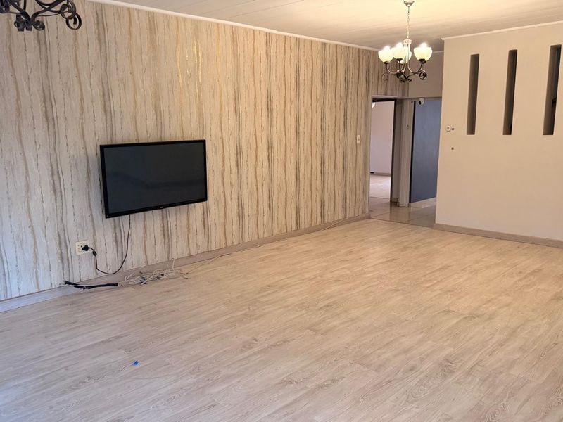 Spacious living area featuring light-toned laminate flooring, textured feature wallpaper, and unique architectural wall niches, providing a bright and versatile living space.
