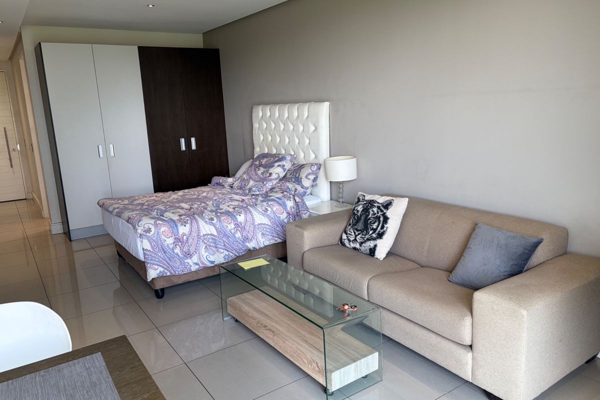 A well-maintained bedroom featuring neutral tiled flooring, recessed ceiling lighting, and a large built-in wardrobe with a modern two-tone finish.