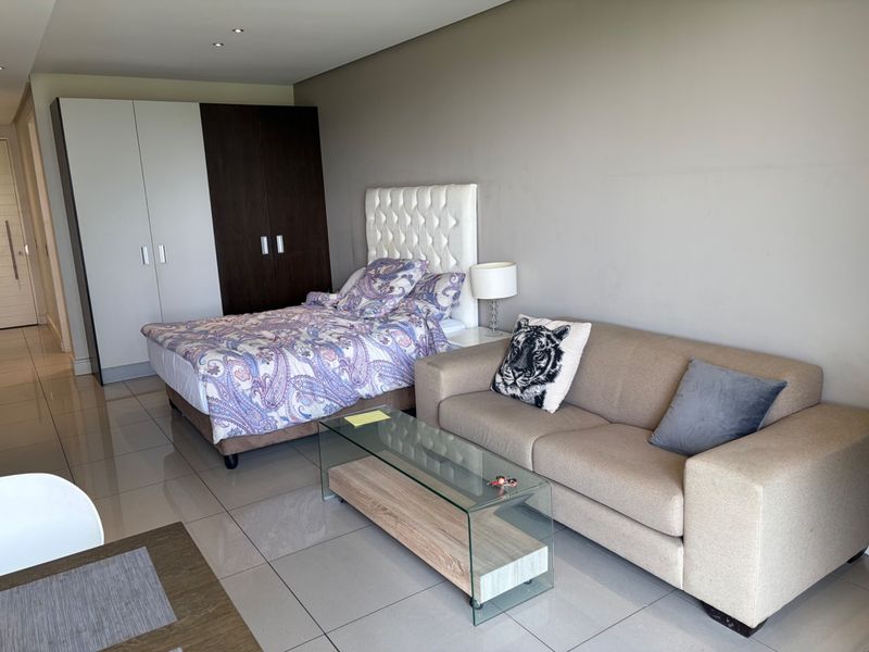 A well-maintained bedroom featuring neutral tiled flooring, recessed ceiling lighting, and a large built-in wardrobe with a modern two-tone finish.