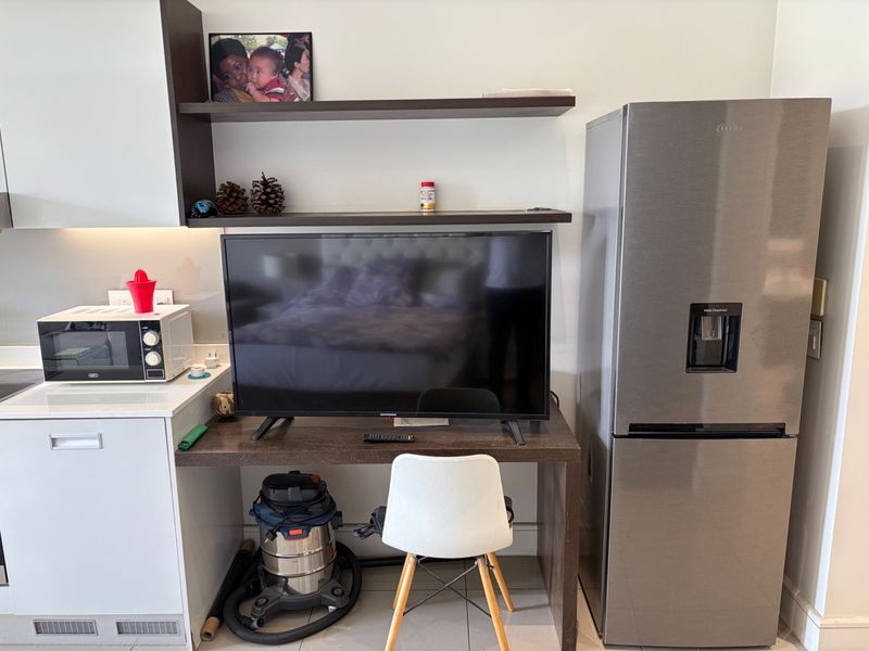 An open-plan living area featuring built-in cabinetry, a dedicated desk space, and modern tiled flooring, providing a functional and compact layout.