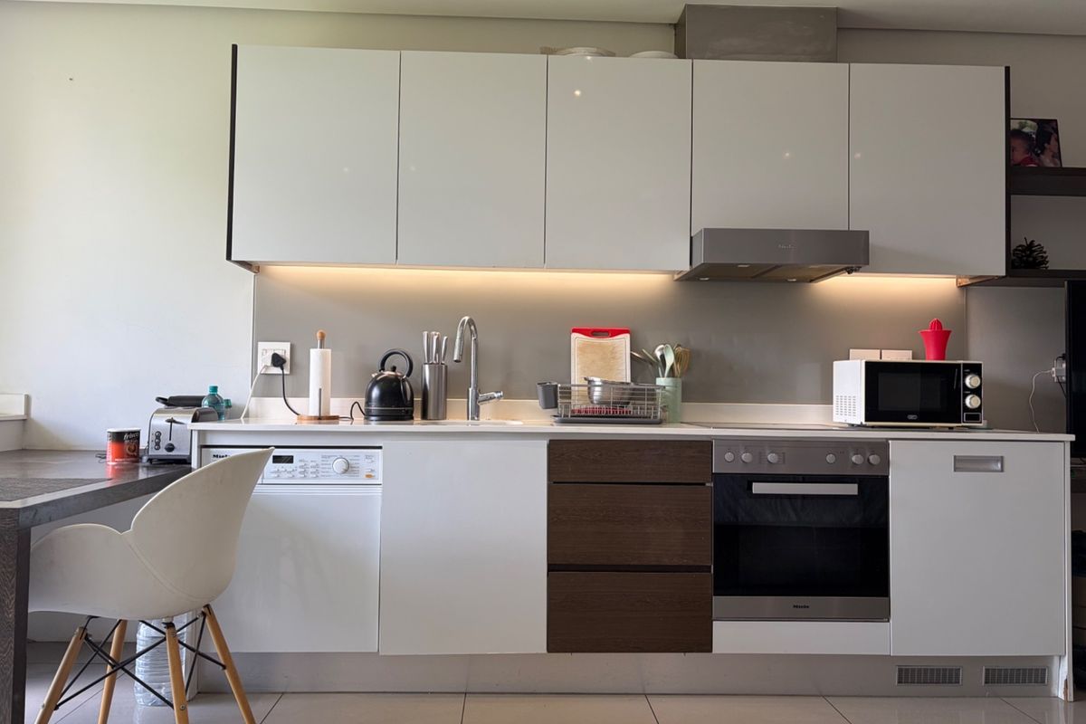 Modern kitchen featuring sleek white and wood-tone cabinetry, integrated appliances, stainless steel oven, extractor fan, and under-cabinet lighting with tiled flooring.