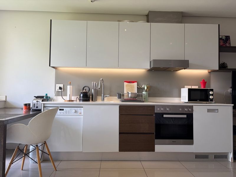 Modern kitchen featuring sleek white and wood-tone cabinetry, integrated appliances, stainless steel oven, extractor fan, and under-cabinet lighting with tiled flooring.