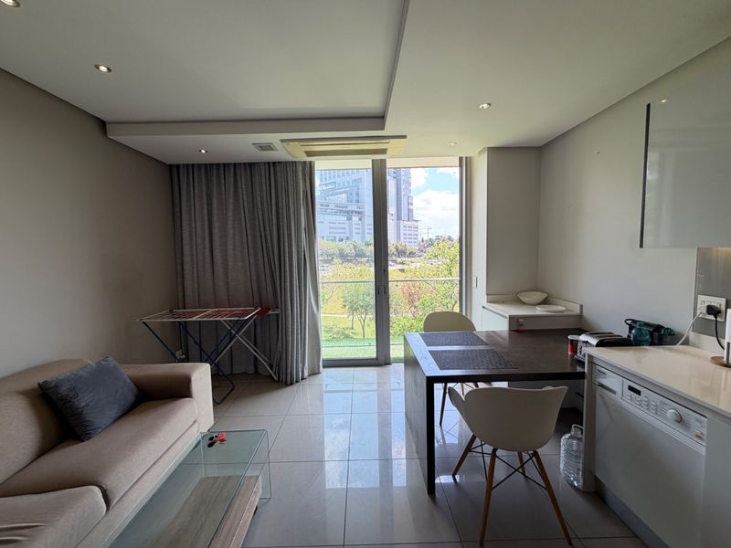 Modern open-plan living area featuring tiled floors, recessed lighting, ducted air conditioning, and a compact kitchen with integrated appliances and balcony access.