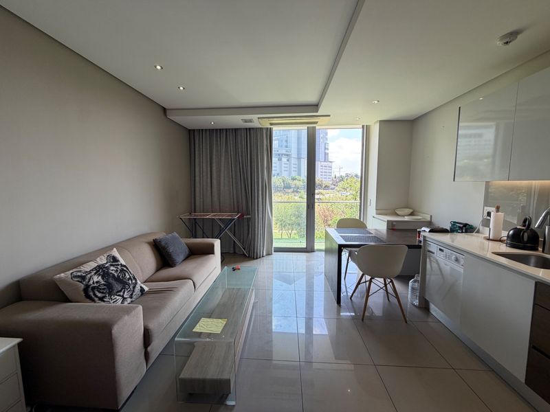 Modern open-plan living area featuring tiled floors, recessed lighting, and a sleek kitchen with integrated appliances, leading to a balcony with scenic views.