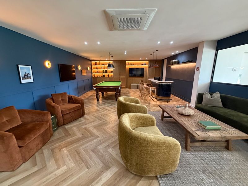 A sophisticated entertainment lounge featuring a built-in bar, pool table, herringbone wood flooring, and elegant wainscoting with integrated lighting.