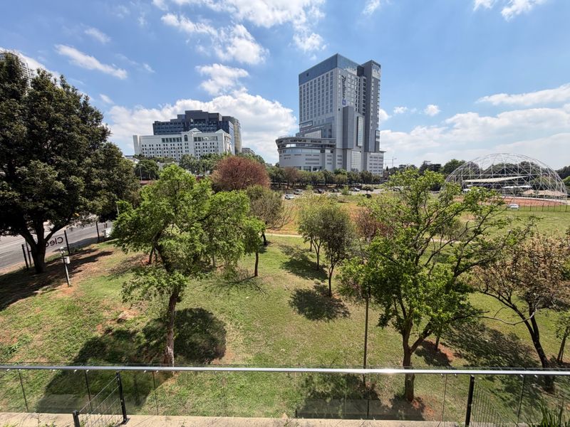 An elevated view overlooking a green park area with urban buildings and a modern high-rise in the background.