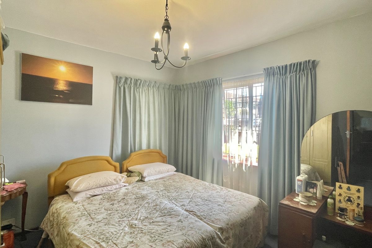 A cozy bedroom featuring a window with security bars and a central ceiling light fixture, offering a functional space with potential for modern updates.