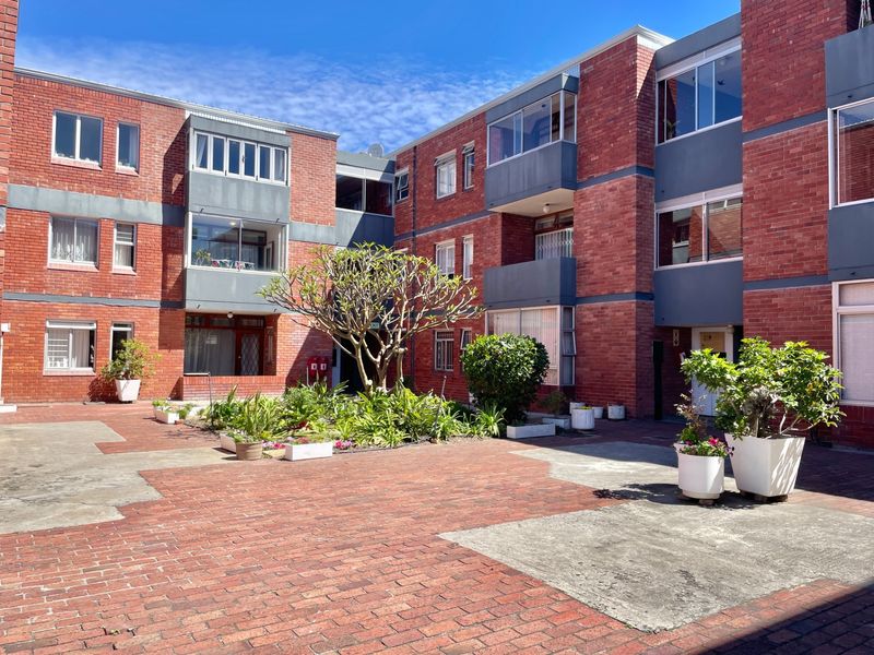A central courtyard area within an apartment complex featuring brick paving, established garden beds, and multi-story brick building facades with enclosed balconies.