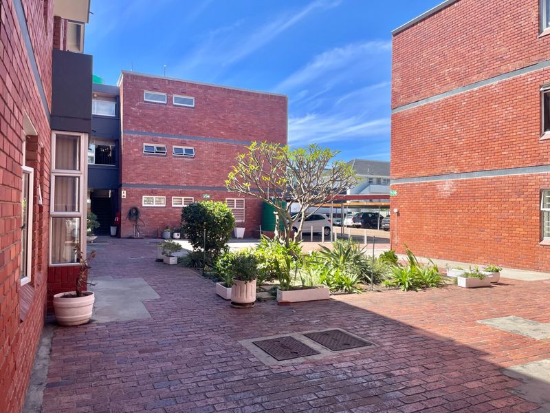 A well-maintained communal courtyard area featuring face brick apartment buildings, paved walkways, and established garden beds.