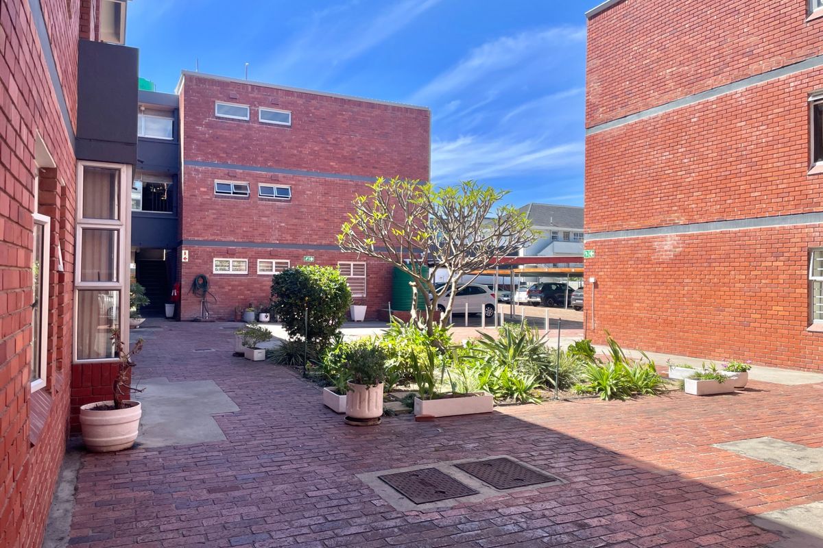 A well-maintained communal courtyard area featuring face brick apartment buildings, paved walkways, and established garden beds.