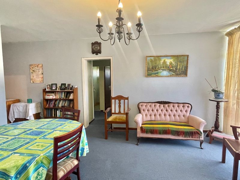 A living room area featuring carpeted flooring and a decorative wrought iron chandelier, providing a functional space with neutral wall finishes.
