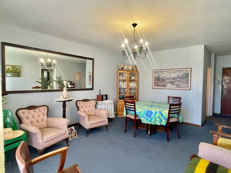 A spacious living and dining area featuring a central chandelier and a large wall-mounted mirror, offering a functional layout for relaxation and dining.