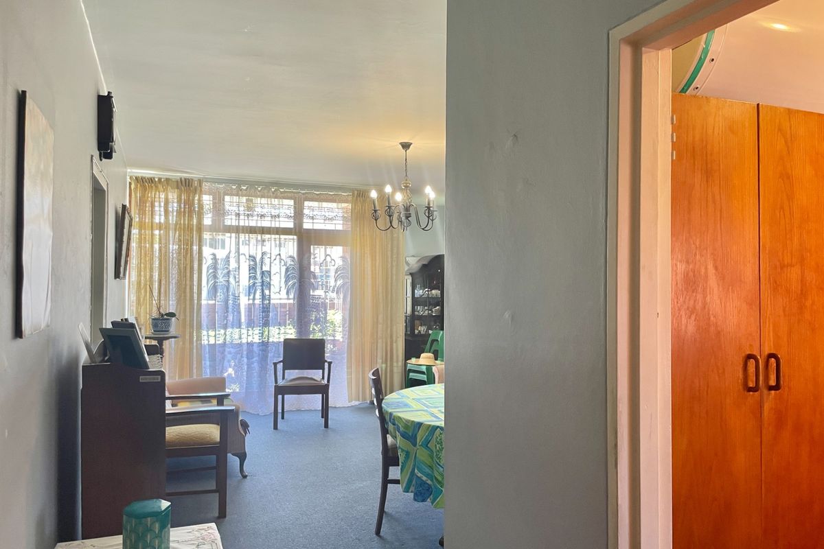 A living and dining area featuring large windows, carpeted flooring, and a classic chandelier, offering a functional space with potential for modernization.