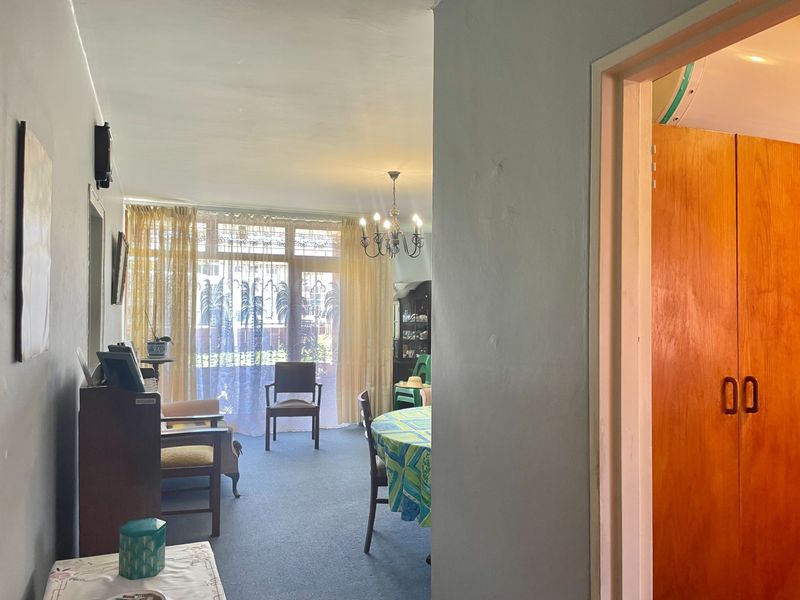 A living and dining area featuring large windows, carpeted flooring, and a classic chandelier, offering a functional space with potential for modernization.