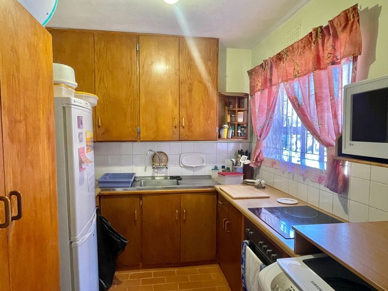 A compact kitchen featuring traditional wooden cabinetry, a stainless steel sink, tiled backsplash, and integrated cooking appliances, offering a functional layout with dated finishes.