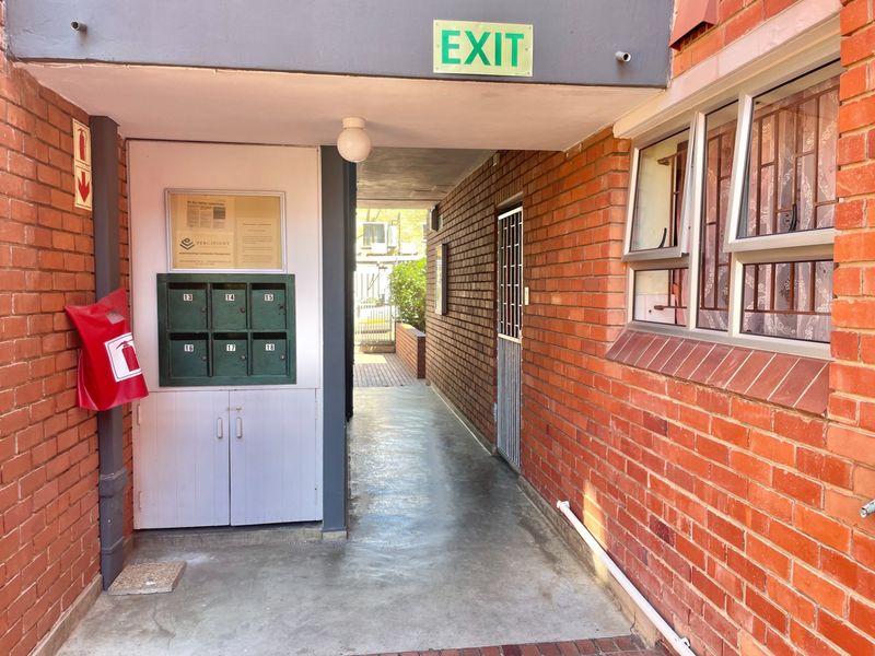 A functional apartment building entrance featuring brick walls, built-in mailboxes, security gates, and essential safety signage.