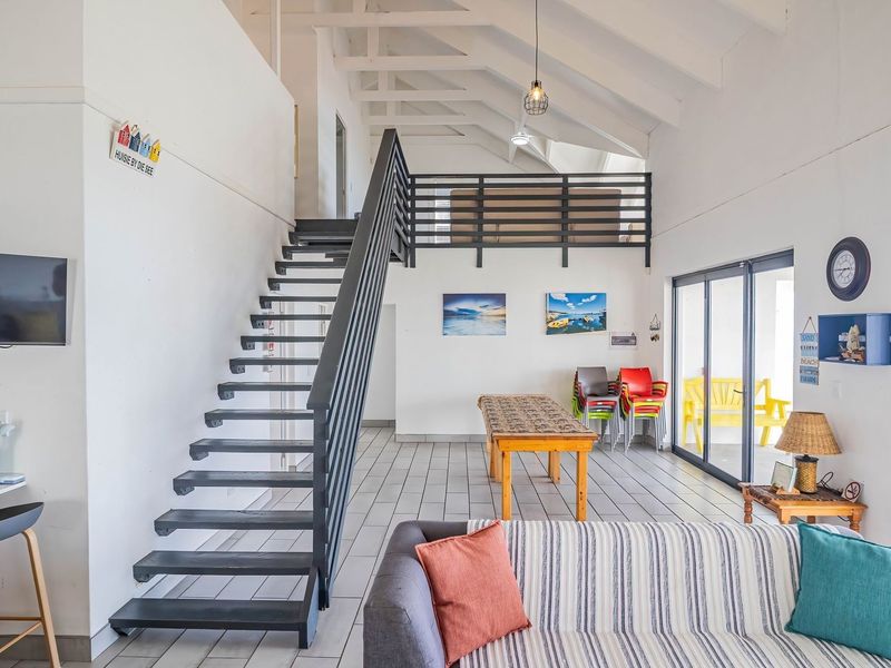 Spacious open-plan living area featuring a modern staircase, vaulted ceilings with exposed rafters, and large sliding doors leading to an outdoor patio.