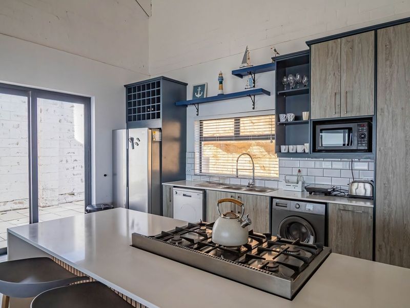 Modern kitchen featuring a central island with gas cooktop, subway tile backsplash, integrated appliances, and direct access to an outdoor patio area.
