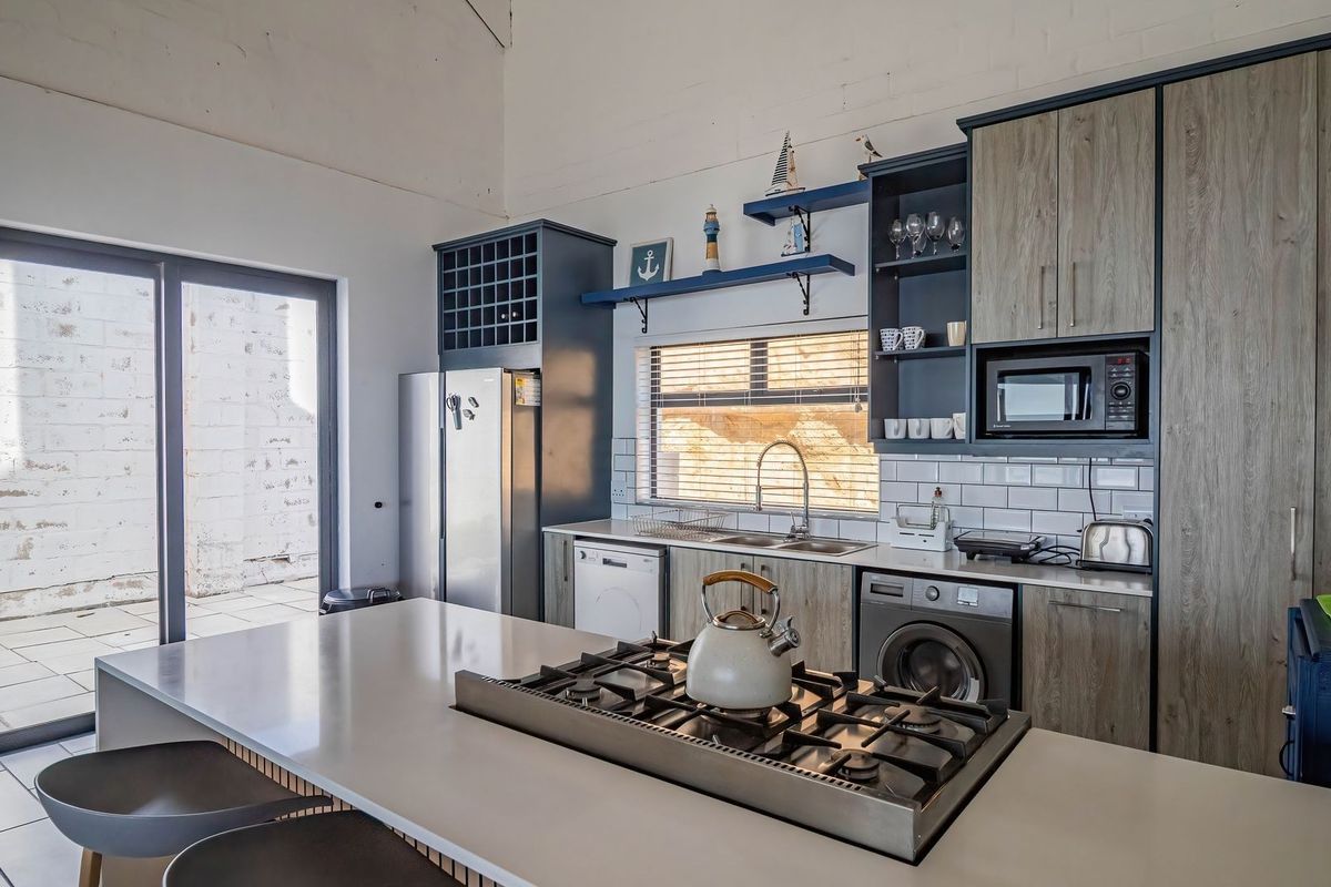 Modern kitchen featuring a central island with gas cooktop, subway tile backsplash, integrated appliances, and direct access to an outdoor patio area.