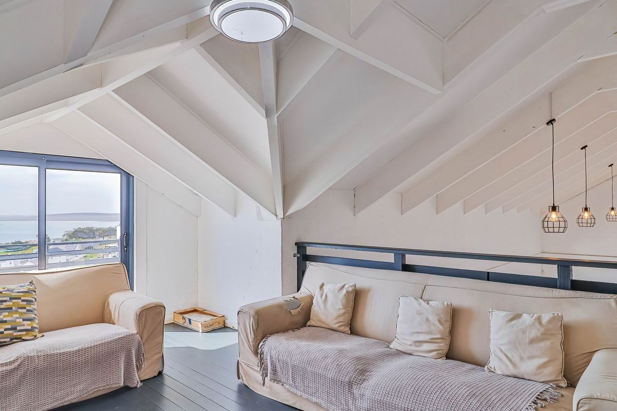 A bright living area featuring a high vaulted ceiling with exposed rafters, modern pendant lighting, and a sliding glass door offering scenic coastal views.