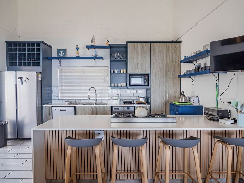 Modern kitchen featuring a central island with gas hob, subway tile backsplash, integrated microwave, and stylish slatted wood cabinetry with ample storage.