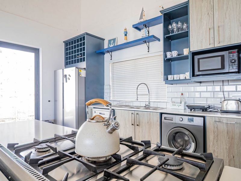 Modern kitchen featuring a gas hob, subway tile backsplash, integrated washing machine, built-in microwave, and stylish blue and wood-grain cabinetry.