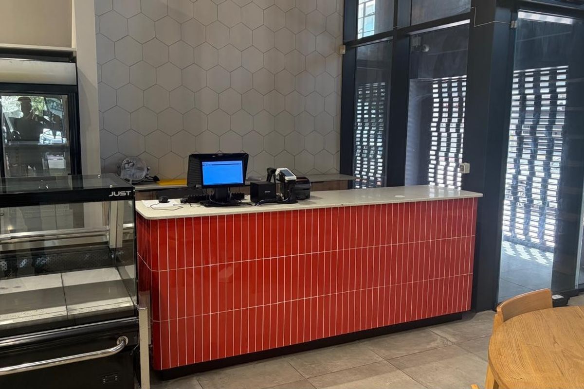 Modern retail space featuring a vibrant red tiled service counter, hexagonal wall accents, and large glass windows providing ample natural light.