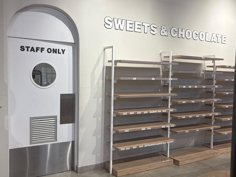 Retail space interior featuring built-in wooden shelving units and a staff-only arched door with a circular window.