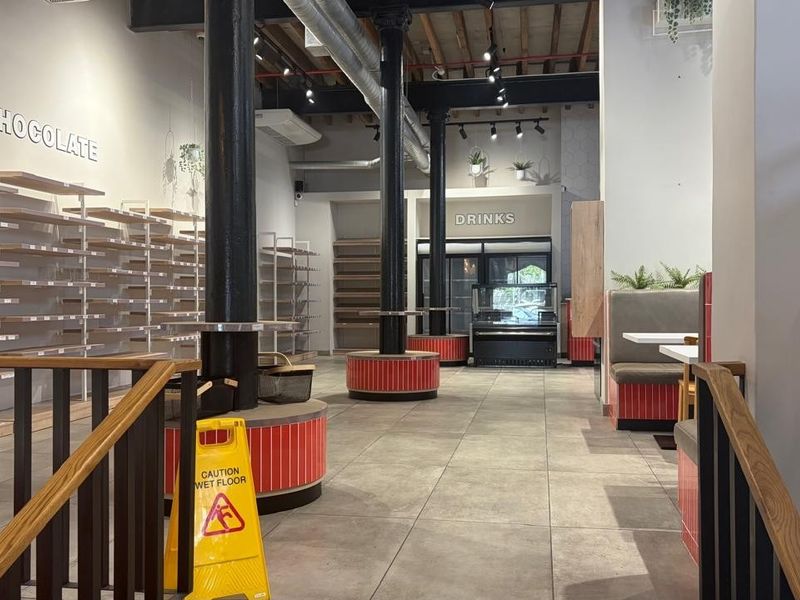Spacious retail interior featuring industrial-style exposed ceilings, cast iron columns, tiled flooring, and integrated shelving and booth seating arrangements.