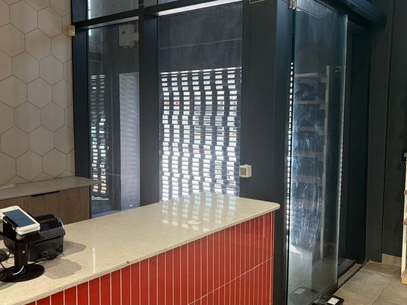 Modern retail space featuring a vibrant red tiled service counter with stone top, hexagonal wall tiling, and large glass storefront with security shutter.