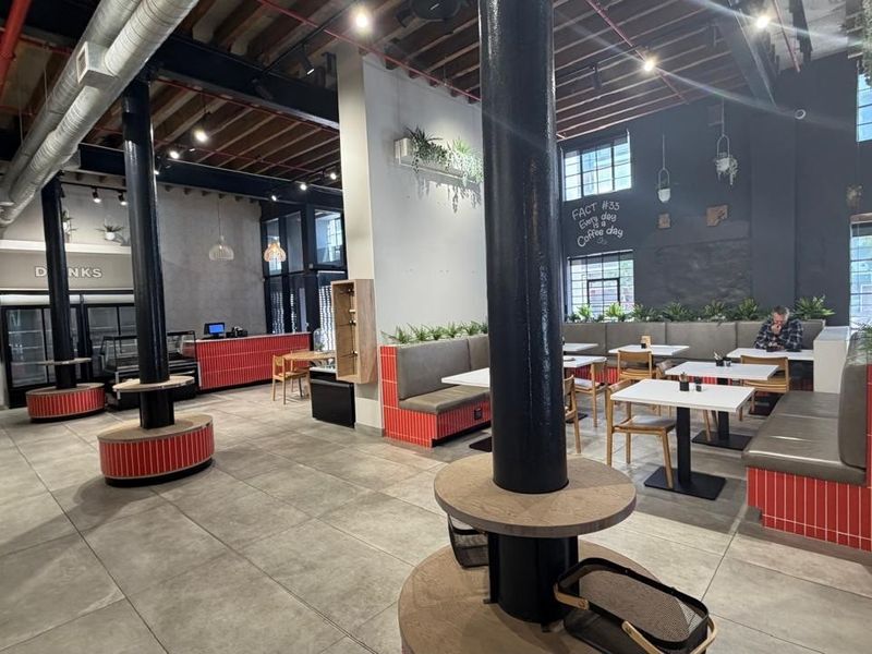 Spacious open-plan retail or cafe interior featuring industrial-style exposed ceilings, structural columns, built-in banquette seating, and modern tiled finishes.