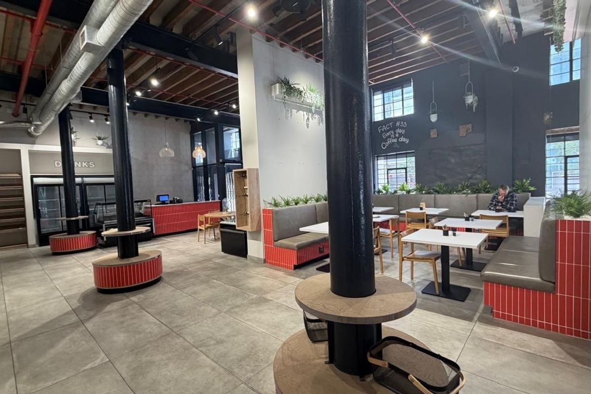 Spacious open-plan retail or cafe interior featuring industrial-style exposed ceilings, structural columns, built-in banquette seating, and modern tiled finishes.