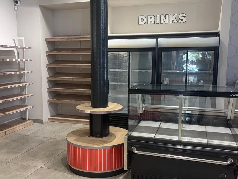 Retail space featuring built-in shelving, commercial refrigeration units, and a central structural column with integrated display base.