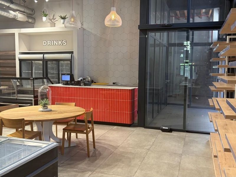 Modern retail space featuring tiled flooring, a vibrant red service counter, built-in refrigeration, and extensive wall-mounted shelving with glass sliding entrance doors.