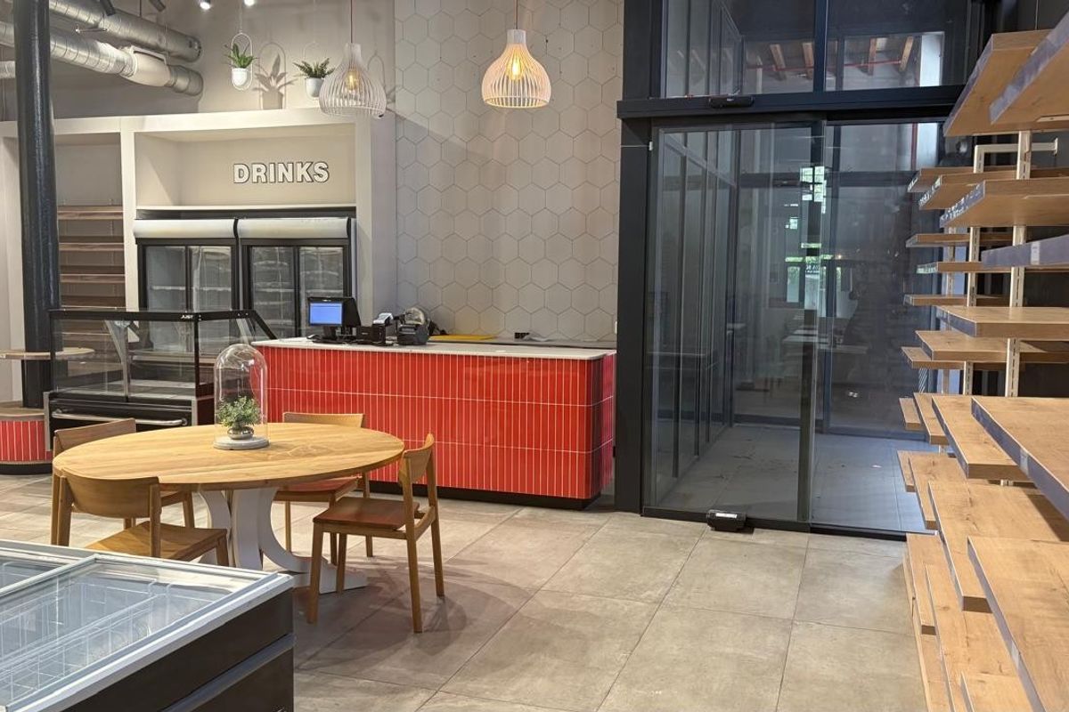 Modern retail space featuring tiled flooring, a vibrant red service counter, built-in refrigeration, and extensive wall-mounted shelving with glass sliding entrance doors.