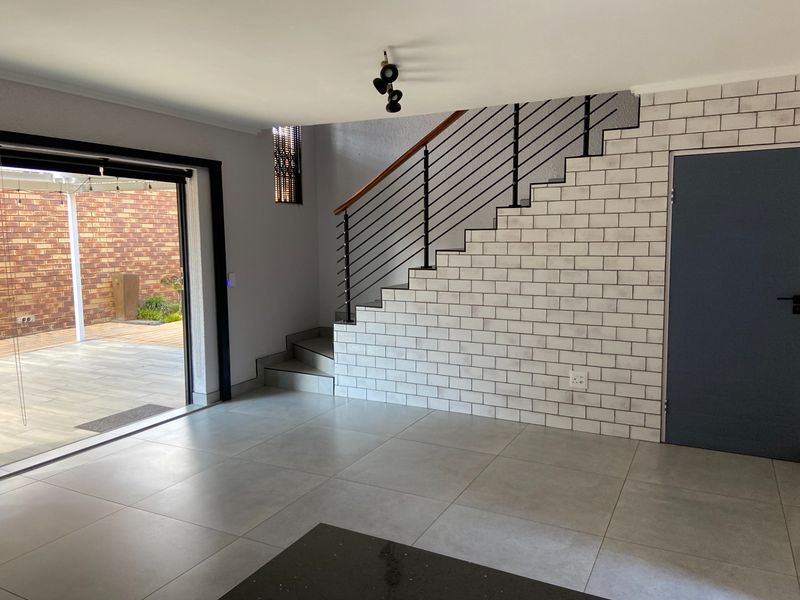 Modern open-plan living area featuring a striking subway tile staircase wall, sleek porcelain flooring, and seamless access to the outdoor patio through sliding doors.