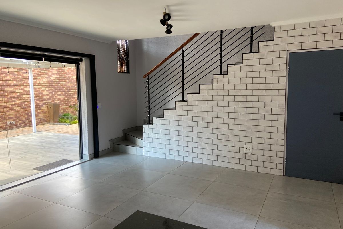 Modern open-plan living area featuring a striking subway tile staircase wall, sleek porcelain flooring, and seamless access to the outdoor patio through sliding doors.