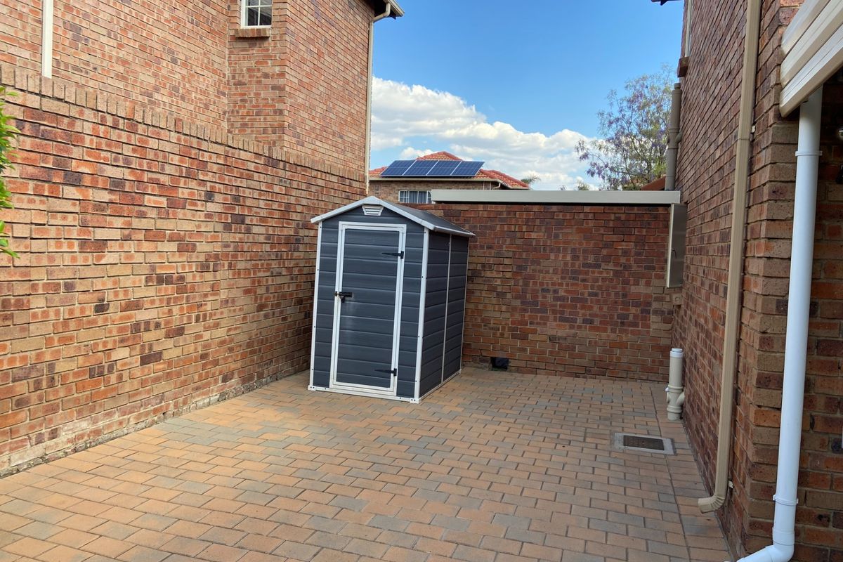 A paved side courtyard area featuring brick boundary walls and a small storage shed.