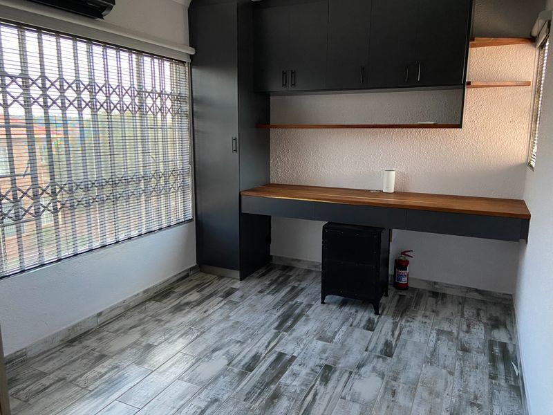 A modern home office featuring built-in cabinetry, a wooden desk surface, tiled flooring, and a security gate on the window.