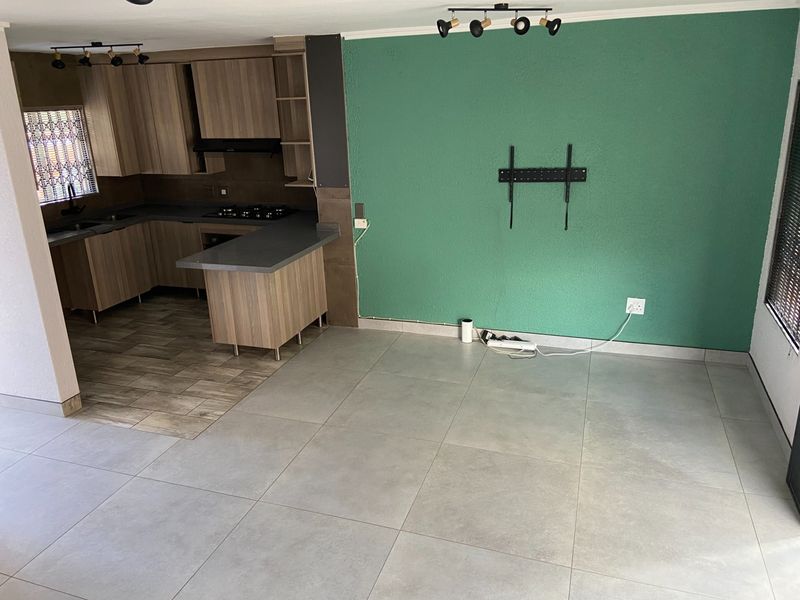 An open-plan living and kitchen area featuring modern tiled flooring, built-in cabinetry with a gas hob, and a vibrant green feature wall.