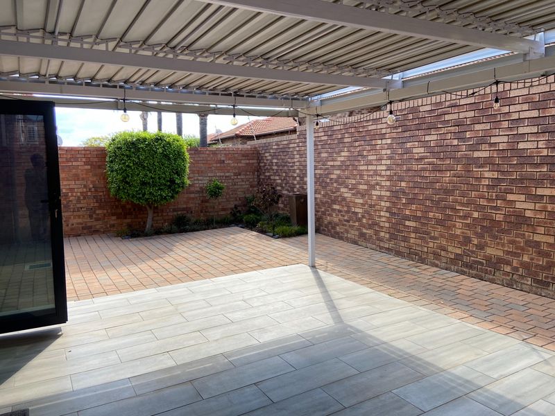 A well-maintained covered patio area featuring paved flooring and enclosed by brick boundary walls, providing a private outdoor space.