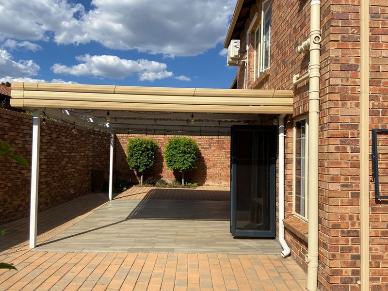 A well-maintained covered patio area featuring brick walls, tiled flooring, and direct access to the rear garden space.