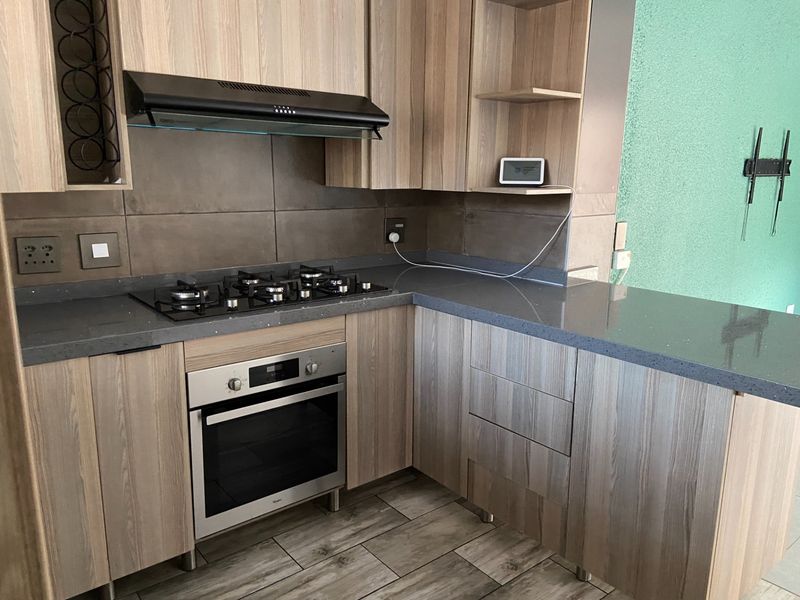 Modern kitchen featuring wood-grain cabinetry, stone countertops, a gas hob, built-in oven, and a sleek tiled backsplash.