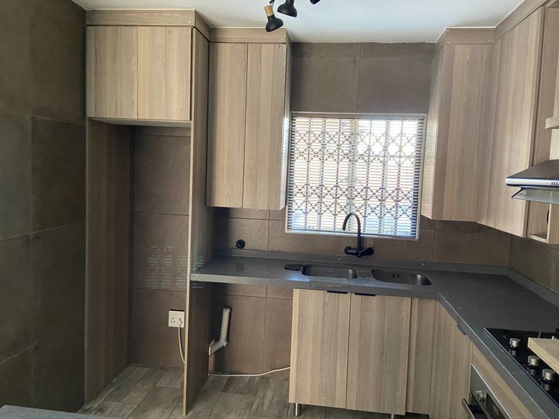 Modern kitchen featuring wood-look cabinetry, stone countertops, integrated appliances, and a double sink with a dark finish mixer tap.