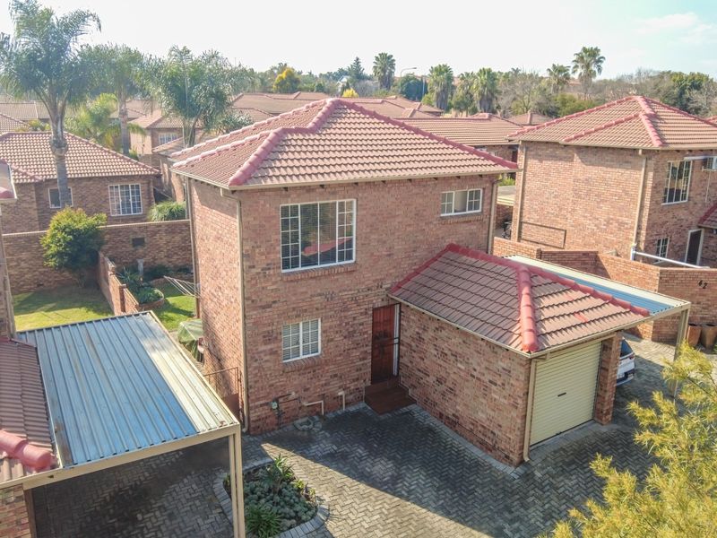 Aerial view of a double-story face-brick house featuring a tiled roof, paved driveway, single garage, and an attached carport within a residential estate.