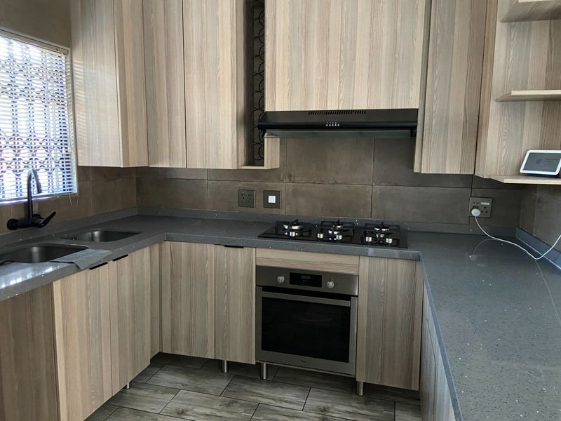 Modern kitchen featuring light wood-grain cabinetry, stone countertops, a gas hob, built-in oven, and a tiled backsplash.