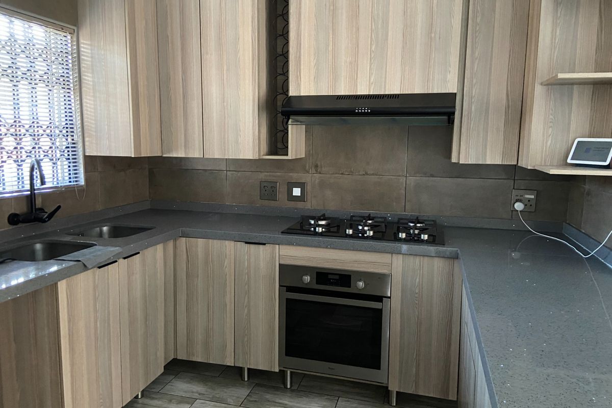 Modern kitchen featuring light wood-grain cabinetry, stone countertops, a gas hob, built-in oven, and a tiled backsplash.