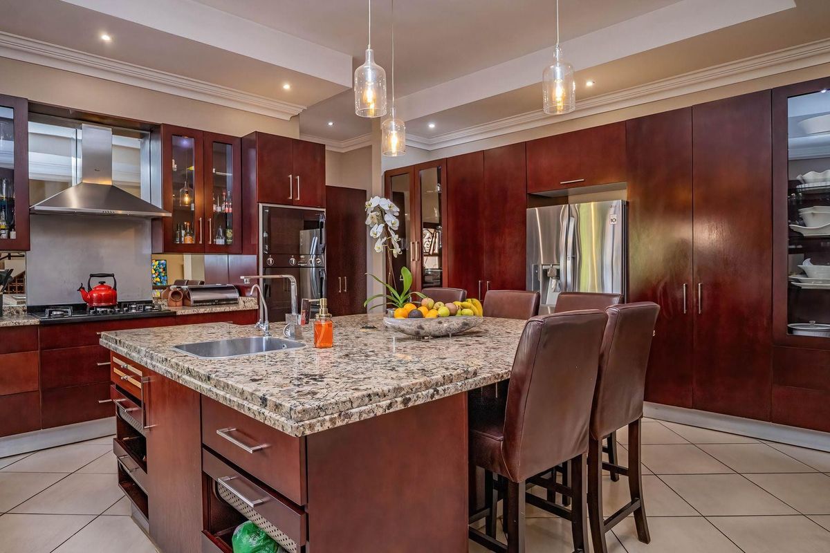 Spacious kitchen featuring dark wood cabinetry, granite countertops, a large central island with sink, and integrated stainless steel appliances.